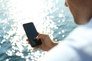 Photo of Man using modern mobile phone near river, closeup