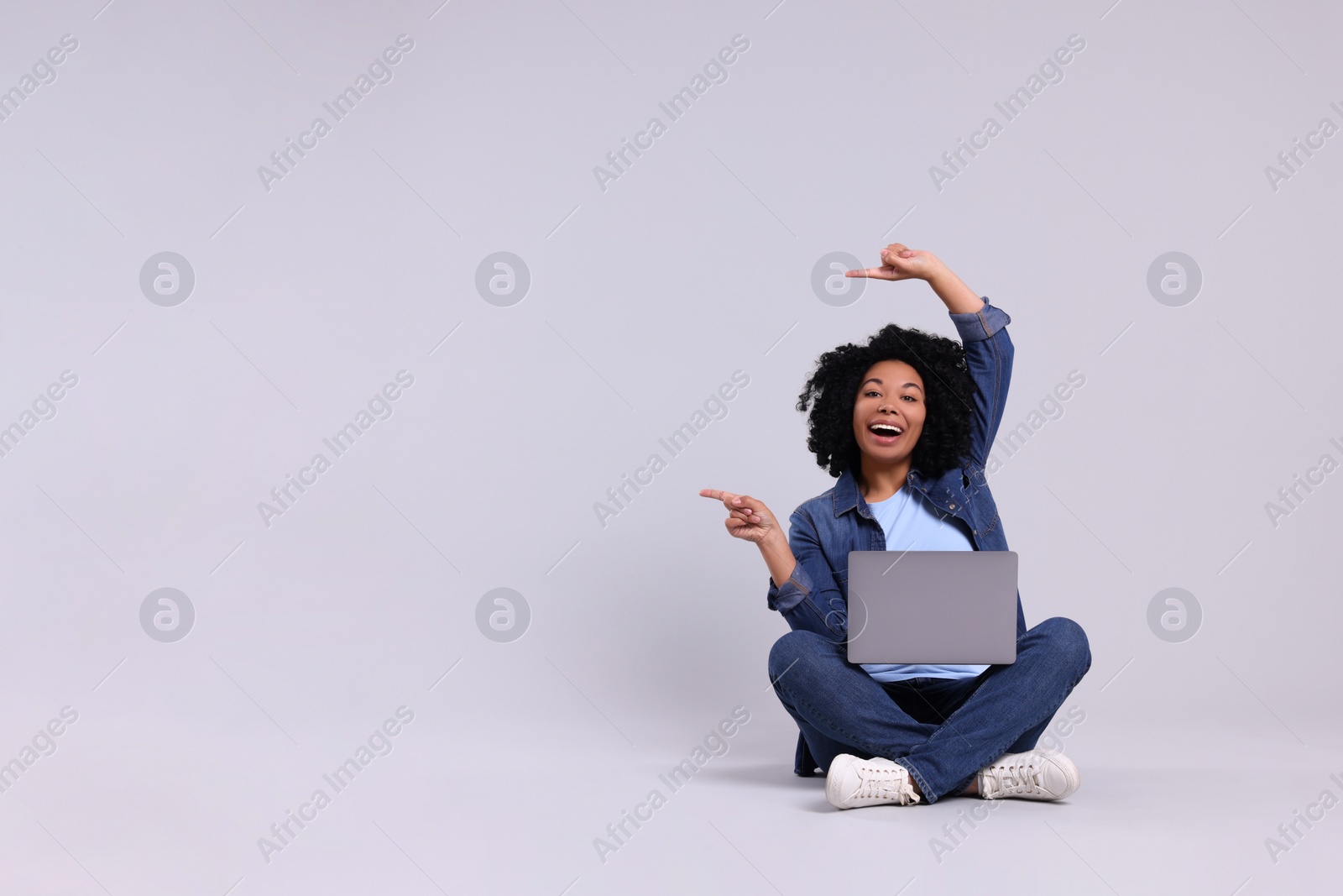 Photo of Happy young woman with laptop pointing at something on light grey background. Space for text