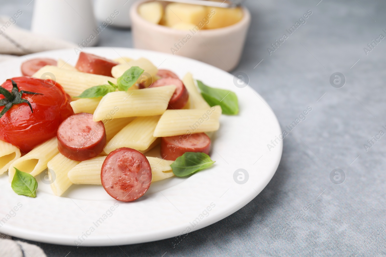 Photo of Tasty pasta with smoked sausage, tomato and basil on light grey table, closeup. Space for text