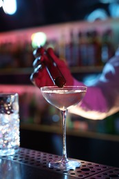 Bartender adding olive into Martini cocktail at bar counter, closeup