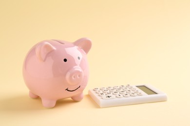 Photo of Financial savings. Piggy bank and calculator on beige background