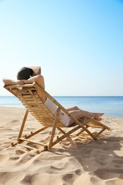 Photo of Young woman relaxing in deck chair on sandy beach