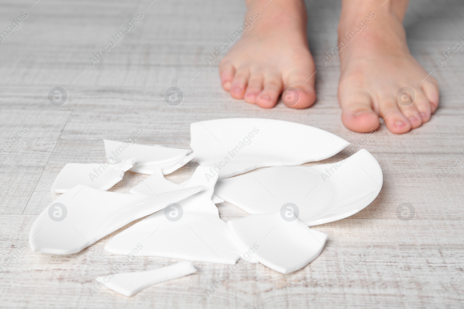 Photo of Barefoot woman standing near broken plate on floor, closeup