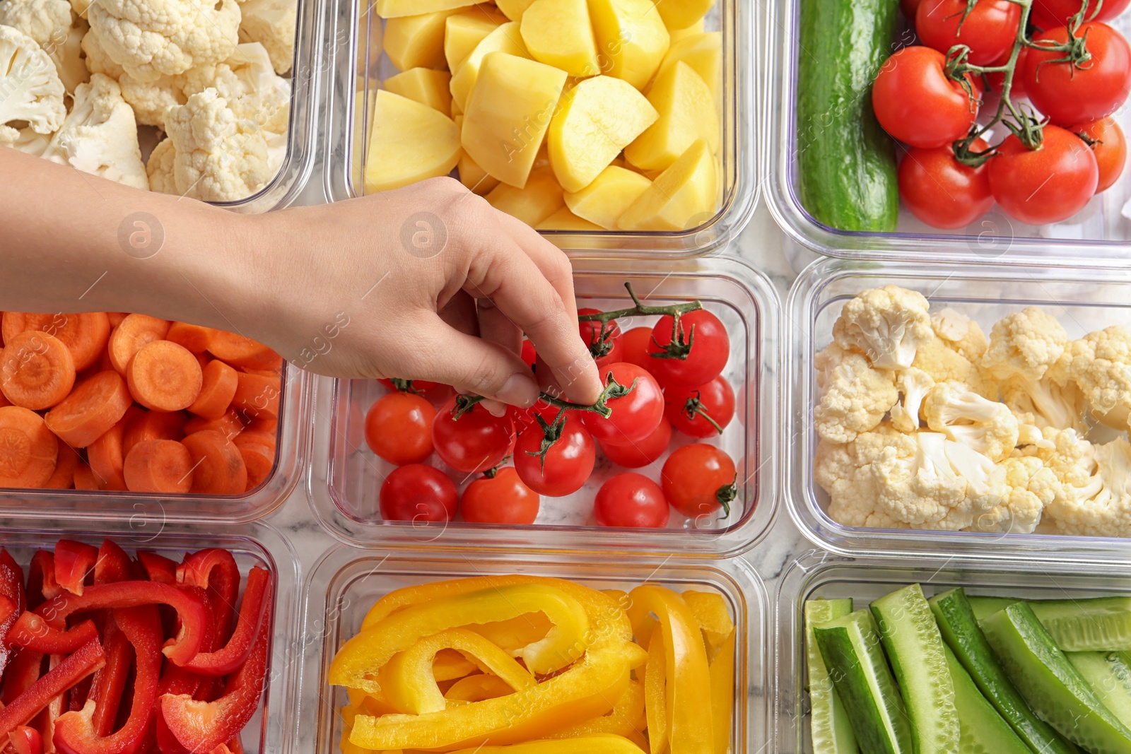 Photo of Woman putting tomatoes into box and containers with raw vegetables, closeup