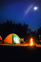 Image of Glowing camping tent near bonfire in wilderness at night