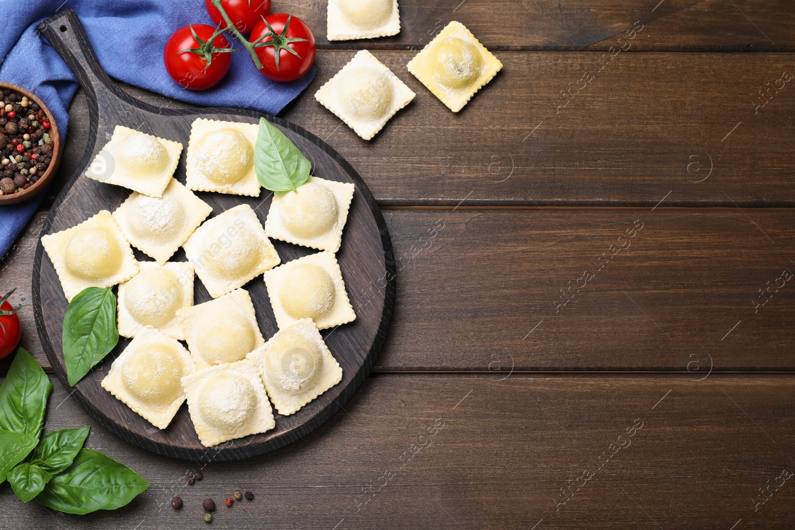 Photo of Uncooked ravioli, basil and tomato on wooden table, flat lay. Space for text