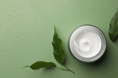 Photo of Glass jar of face cream and leaves on wet green surface, flat lay. Space for text