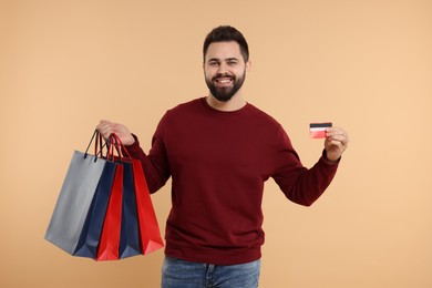 Photo of Smiling man with many paper shopping bags showing credit card on beige background