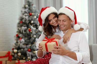 Image of Happy couple in Santa hats with Christmas gift at home