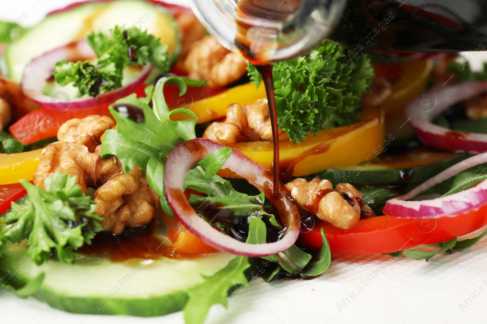 Photo of Pouring balsamic vinegar onto vegetable salad, closeup