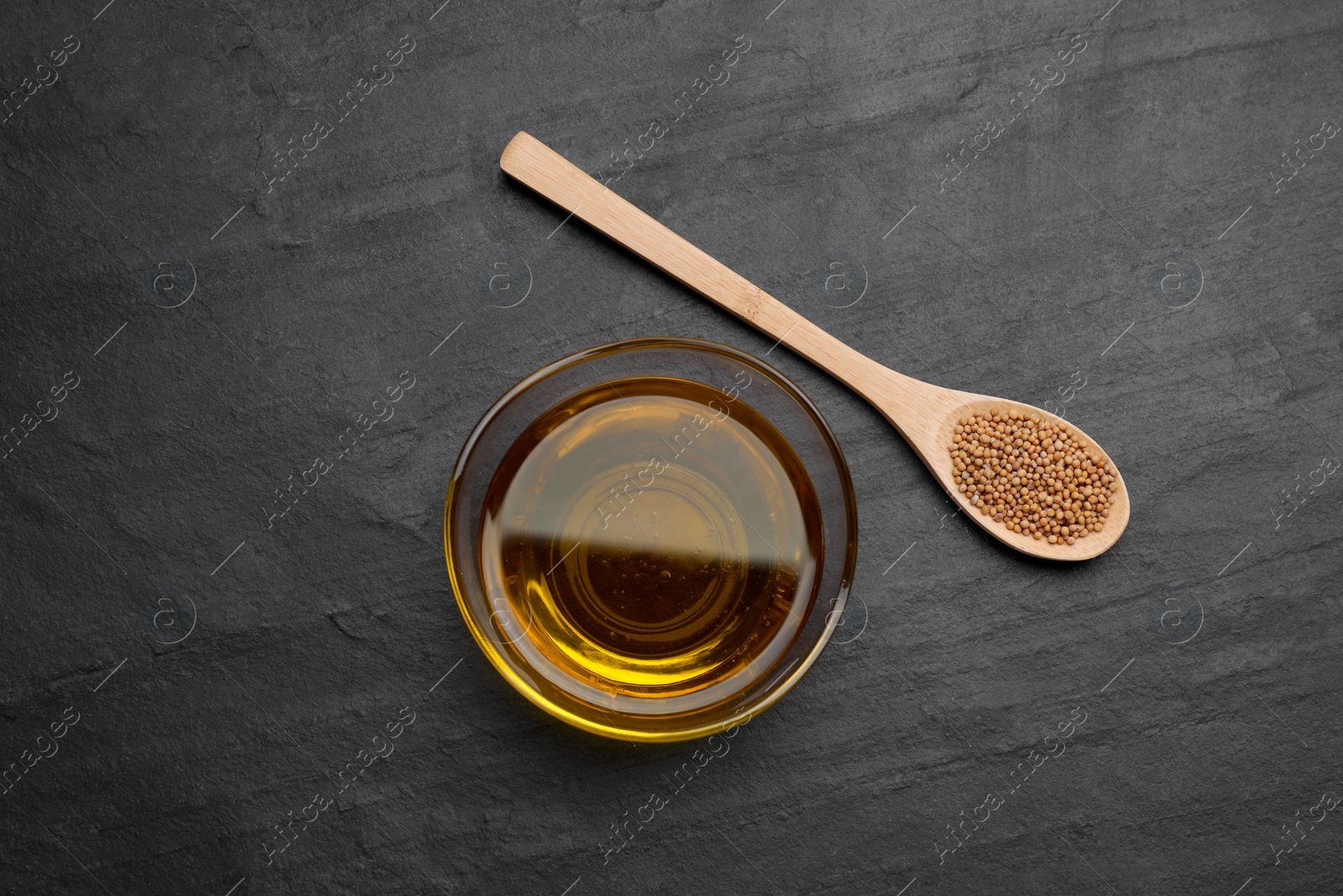Bowl of natural oil and spoon with mustard seeds on black table, flat lay Photo of Bowl of natural oil and spoon with mustard seeds on black table, flat lay