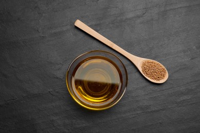 Photo of Bowl of natural oil and spoon with mustard seeds on black table, flat lay