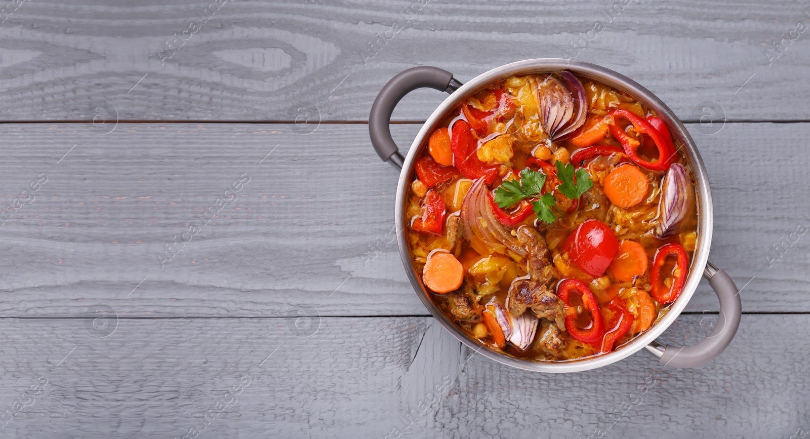 Photo of Saucepan of delicious vegetable soup with meat and ingredients on grey wooden table, top view. Space for text