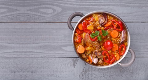 Saucepan of delicious vegetable soup with meat and ingredients on grey wooden table, top view. Space for text