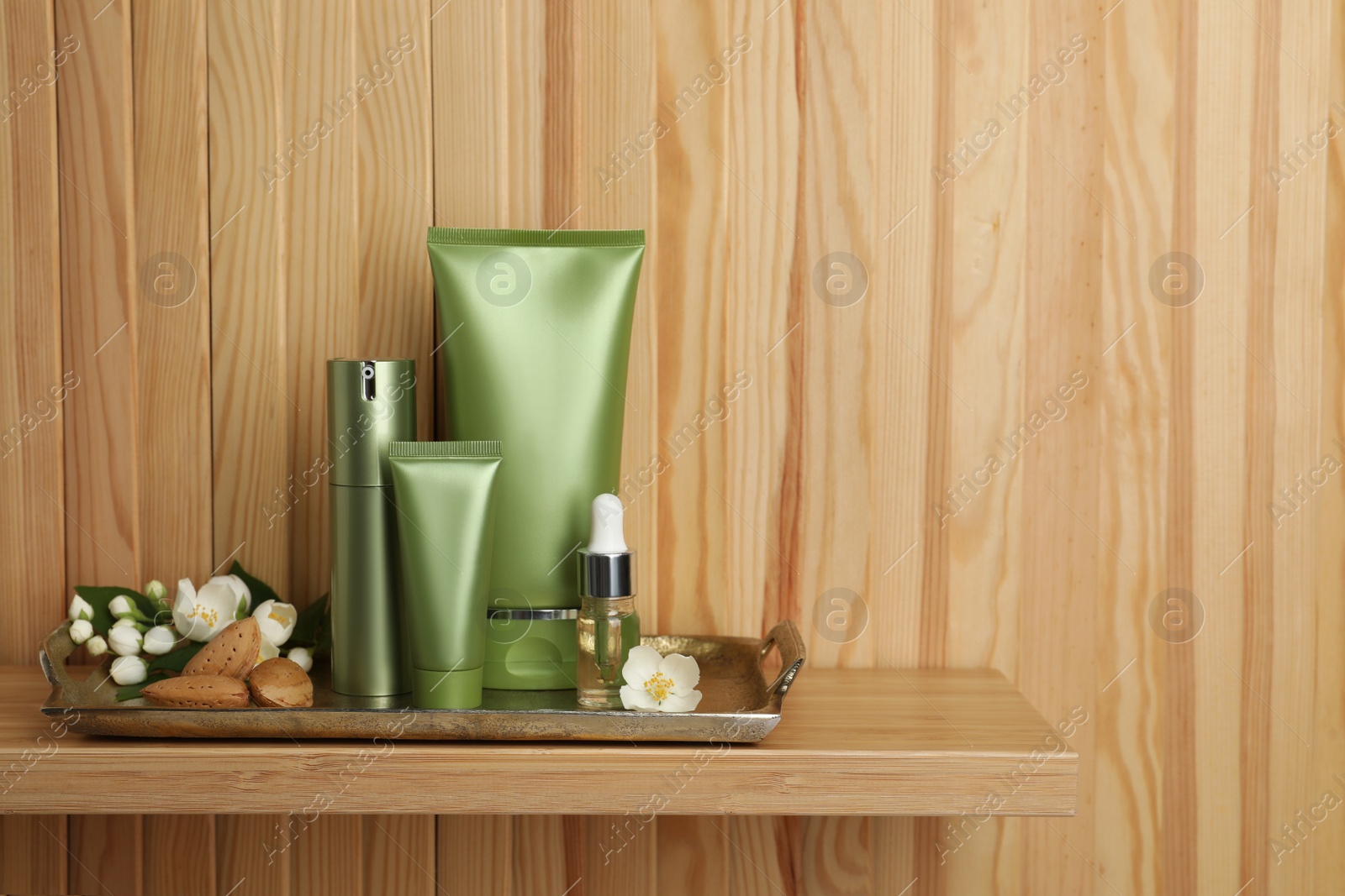 Photo of Set of cosmetic products, almond nuts and flowers on shelf near wooden wall