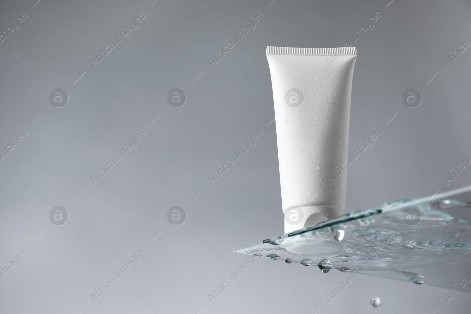 Photo of Tube with moisturizing cream on glass against grey background, low angle view. Space for text