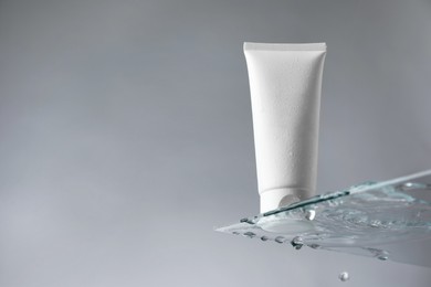 Tube with moisturizing cream on glass against grey background, low angle view. Space for text