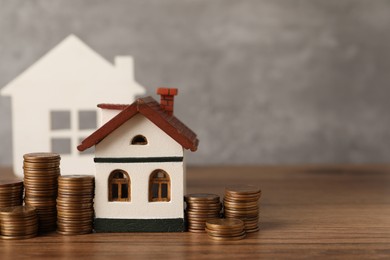 House models and stacked coins on wooden table against gray background, space for text