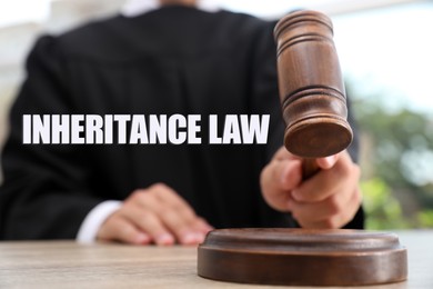 Image of Phrase Inheritance law and judge with gavel at wooden table indoors, closeup