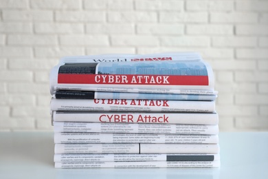 Photo of Newspapers with headlines CYBER ATTACK stacked on  table near white brick wall