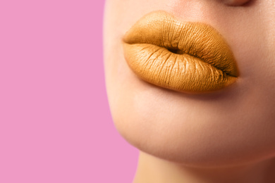 Woman with golden lipstick on pink background, closeup