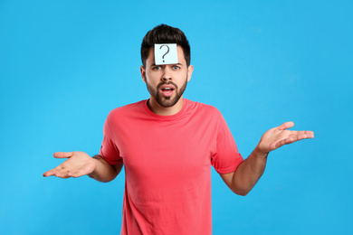 Emotional young man with question mark sticker on forehead against light blue background