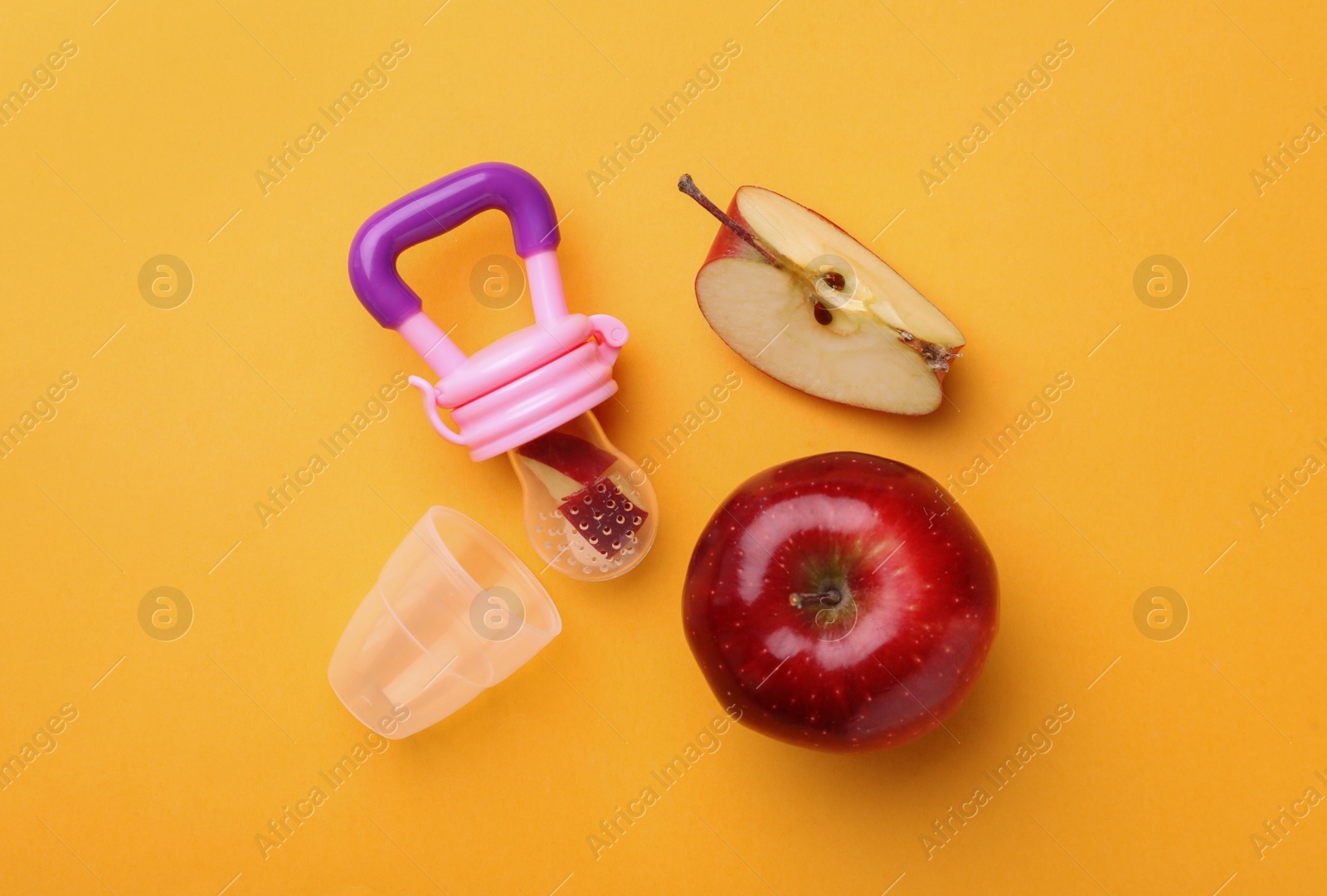 Photo of Nibbler with fresh apple on yellow background, flat lay. Baby feeder
