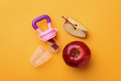 Nibbler with fresh apple on yellow background, flat lay. Baby feeder