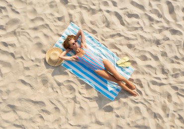 Woman sunbathing on beach towel at sandy coast, aerial view