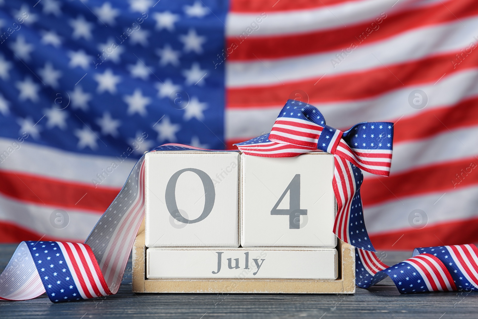 Photo of Wooden calendar with bow on table against USA flag. Happy Independence Day