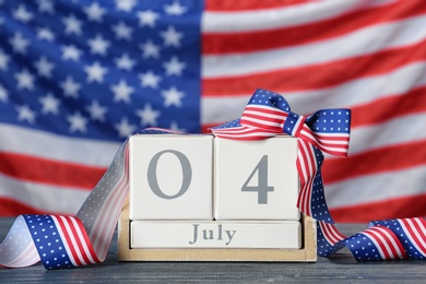 Wooden calendar with bow on table against USA flag. Happy Independence Day