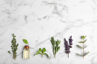 Photo of Essential oil in glass bottle, herbs and space for text on marble background, flat lay