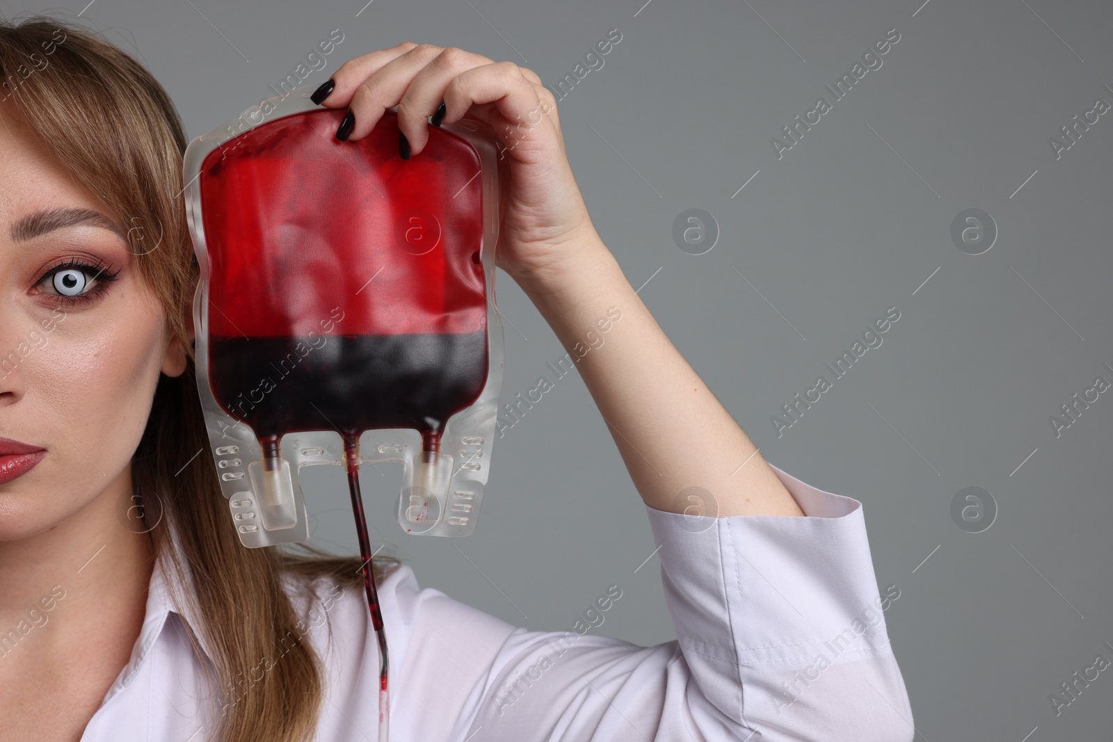 Photo of Woman in scary nurse costume with blood bag on light grey background, closeup and space for text. Halloween celebration