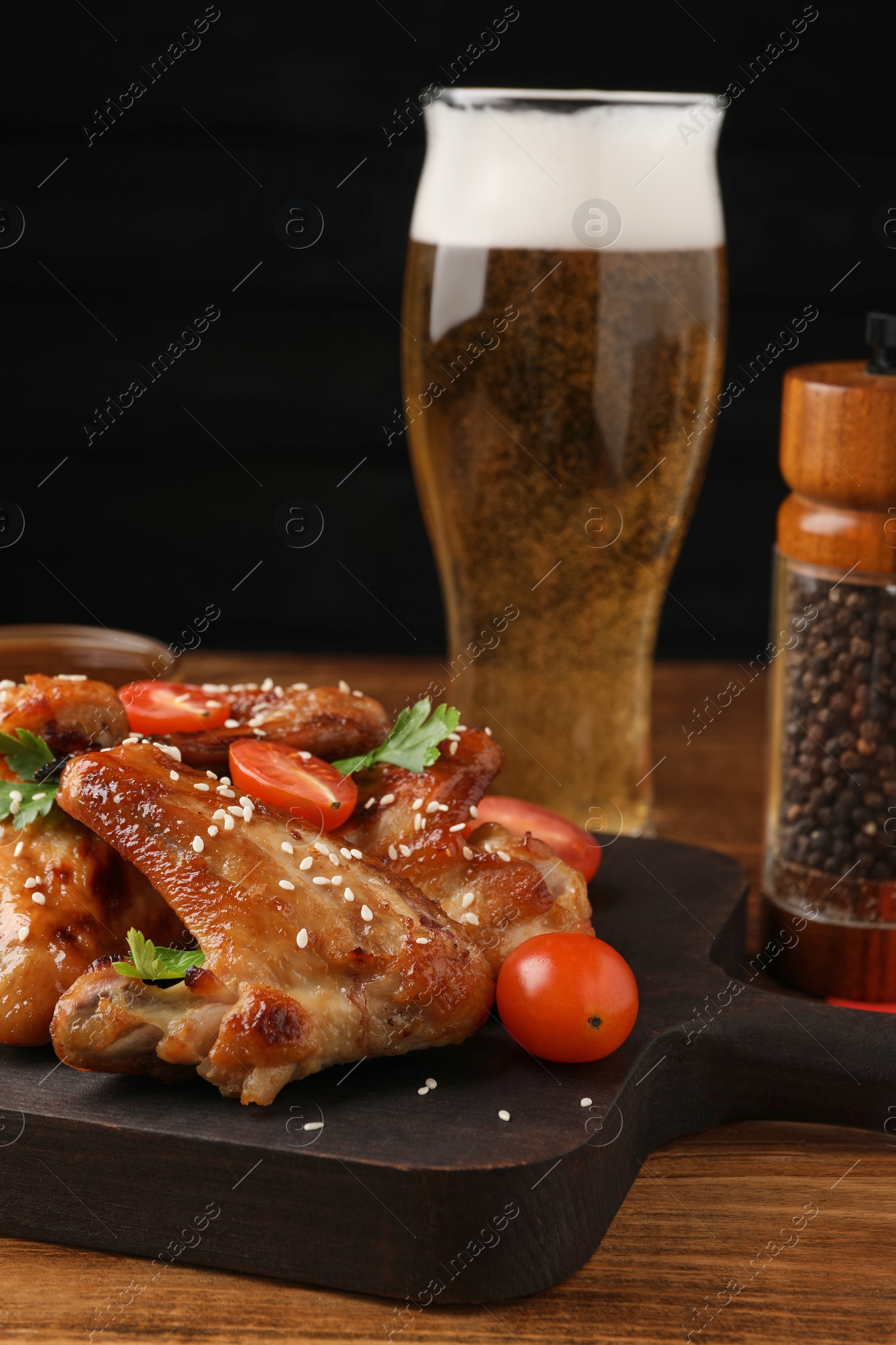 Photo of Glass of beer and delicious baked chicken wings with ingredients on wooden table