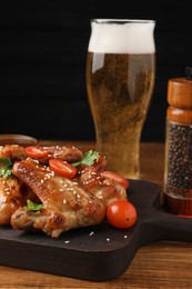Glass of beer and delicious baked chicken wings with ingredients on wooden table