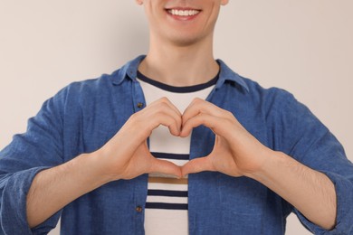 Photo of Happy volunteer making heart with his hands on light background, closeup