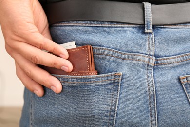 Photo of Man putting wallet with money into pocket of jeans, closeup