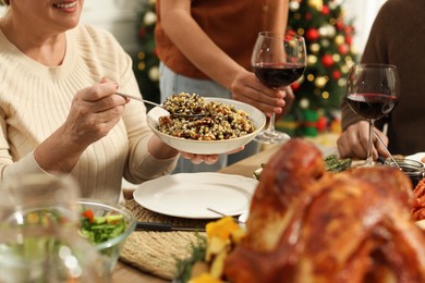 Photo of Woman with bowl of traditional Christmas kutia and her family at festive dinner, closeup. Slavic dish