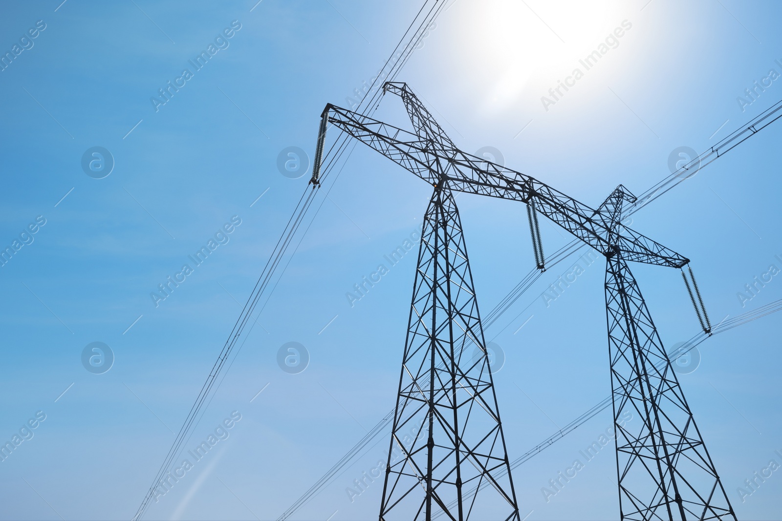 Photo of High voltage tower with electricity transmission power lines against blue sky, low angle view