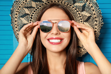 Image of Young woman wearing stylish sunglasses with reflection of mountains and hat on blue wooden background 