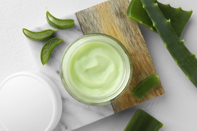 Jar with cream and cut aloe leaves on white table, flat lay