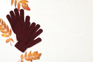 Stylish woolen gloves and dry leaves on white wooden table, flat lay. Space for text