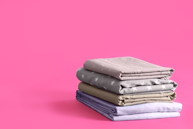 Photo of Stack of clean bed sheets on pink background. Space for text