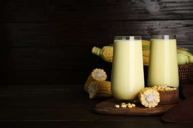 Tasty fresh corn milk in glasses and cobs on wooden table. Space for text