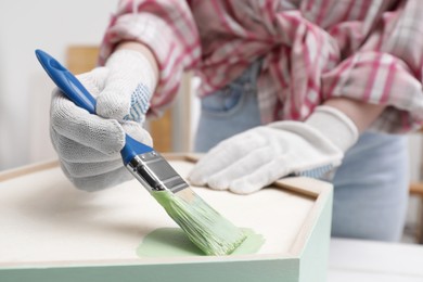 Photo of Woman painting honeycomb shaped shelf with brush indoors, closeup