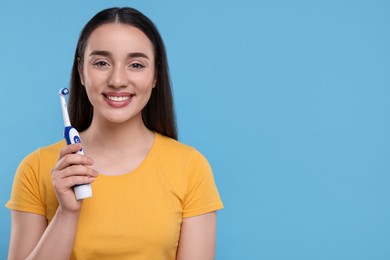 Photo of Happy young woman holding electric toothbrush on light blue background, space for text
