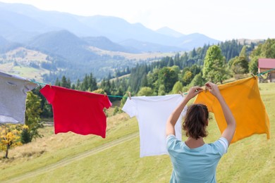 Photo of Woman hanging clean laundry with clothespins on washing line in mountains, back view