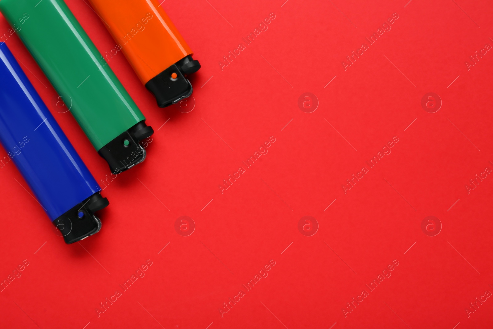 Photo of Stylish small pocket lighters on red background, flat lay. Space for text