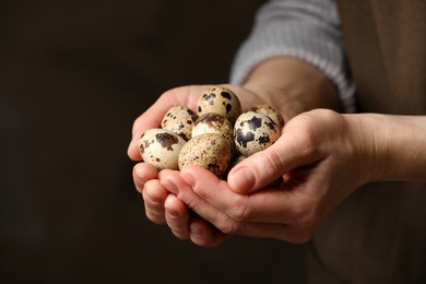 Photo of Woman with handful of quail eggs on dark background, closeup