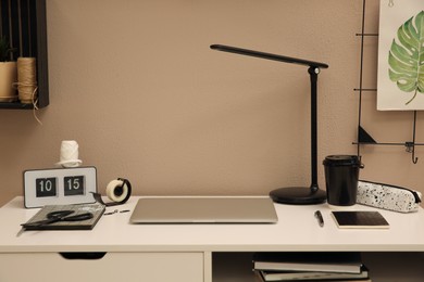 Photo of Stylish workplace with laptop on white desk near beige wall. Interior design